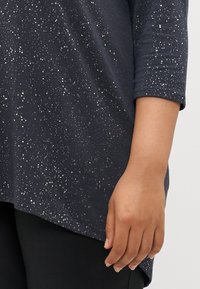 Sötét tengerészkék, háromnegyedes ujjú felső, amelyen fehér pettyek szétszórva találhatóak, puha, textúrált anyagból készült.