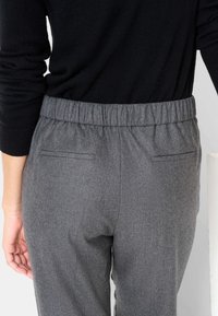 Pantalon à taille élastique grise avec une texture lisse, doté de deux poches arrière, conçu pour le confort et la facilité de port.