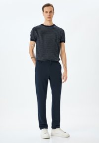 Gestreept donkerblauw t-shirt met ronde hals, gecombineerd met donkerblauwe broek. Het model draagt witte sneakers. Focus op een casual, op maat gemaakte pasvorm en een soepele textuur.