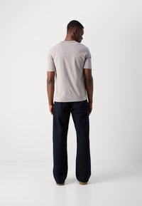 Gray short-sleeve t-shirt with a crew neckline, paired with dark wide-leg pants and tan shoes, viewed from the back.