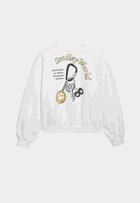 Sweatshirt blanc avec des manches bouffantes. Imprimé graphique comprenant des clés, un visage souriant, et du texte : "Smiley World" et "Destination sans regrets."