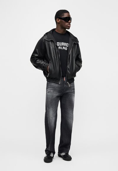 Fekete bőr pilóta dzseki, fekete grafikus póló, kopott szürke farmer szakadt részletekkel, és fekete tornacipő fehér csíkokkal.