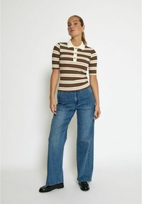 Brun och krämrandig polotröja med krage, korta ärmar och knappar. Kombinerad med lösa blå denimjeans och svarta skor.