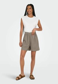 Top bianco senza maniche abbinato a pantaloni corti marroni a vita alta. Tessuto morbido, vestibilità rilassata e vita arricciata. Sandali marroni completano l'outfit.