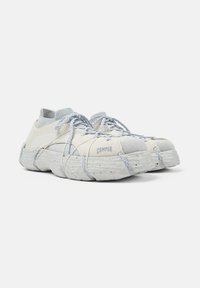 Sneaker beige lavorati a maglia con suole spesse e testurizzate, colli elastici alla caviglia e unici lacci a loop avvolti intorno alle scarpe.
