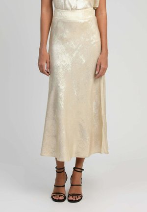 Jupe midi crème brillante portée avec des sandales noires à talons hauts et à brides, vue de la taille aux pieds sur le mannequin.