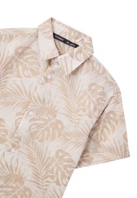 Camicia a maniche corte in tessuto beige chiaro, con un motivo di foglie di palma in tonalità beige più scure. Con colletto e bottoni bianchi.