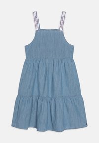 Světle modré denimové šaty s nastaviteln�ými ramínky, rozšířenou volánkovou sukni a logem na ramínkách. Jednoduchý A-liniový design, každodenní styl.