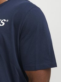 Camiseta de algodón azul marino con cuello redondo y mangas cortas. Presenta un logo blanco impreso en el pecho y una textura suave.