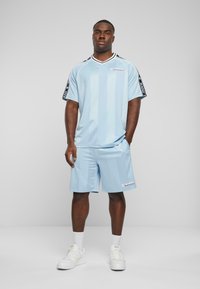 Světle modrý sportovní dres a šortky s vertikálními pruhy, černé akcenty na rukávech a detail loga. Nosené s bílými teniskami.