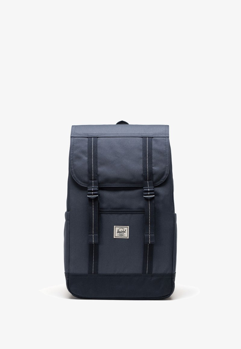 Námorníková látková batoh s uzávěrem na klapku, dvěma nastavovacími popruhy, přední kapsou a obdélníkovým tvarem. Obsahuje bílé švy a logo nášivku.