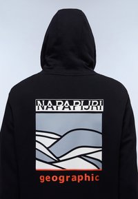 Svart hoodie med en grafik på baksidan, prydd med ljusblå och grå vågmönster, "NAPAPURI"-text ovanför och "geographic" i orange nedanför.
