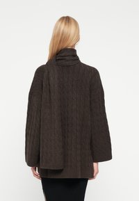 Brun stickad tröja med hög krage, texturerat mönster och lång, draperad sjaldetalj. Långa ärmar och ribbad fåll.