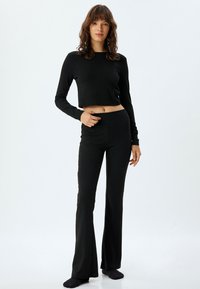Top negro de manga larga recortado combinado con pantalones negros acampanados, ambos en una tela suave y elástica. Diseño simple sin patrones visibles.