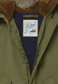 Oliwkowa kurtka z futrzanym kołnierzem w kolorze brązowym, granatowe wnętrze i metką J.Crew. Posiada zamek błyskawiczny z przodu oraz akcenty w postaci guzików.