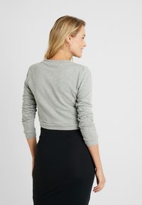Sweatshirt cinzento, curto, com mangas longas, decote redondo e punhos canelados, combinado com uma saia justa preta. Tecido macio e texturizado.
