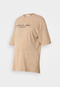 Beige krāsā pārspīlēts t-krekls, izgatavots no mīksta kokvilnas auduma, ar apaļu dekoltē un īsām piedurknēm. Priekšpusē ir melnā krāsā drukāts teksts "C'est le Mini Club Mama".