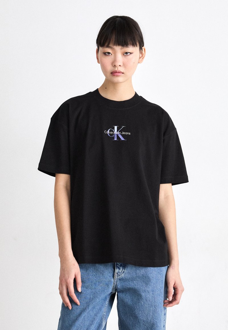 Crna pamučna majica s opuštenim krojem, rebrastim okruglim izrezom i središnjim grafičkim logom u ljubičastoj i bijeloj boji koji glasi "Calvin Klein Jeans".