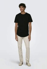 T-shirt preto de manga curta com gola redonda, combinado com calças retas bejes claras e ténis bejes. Design simples, sem padrões.