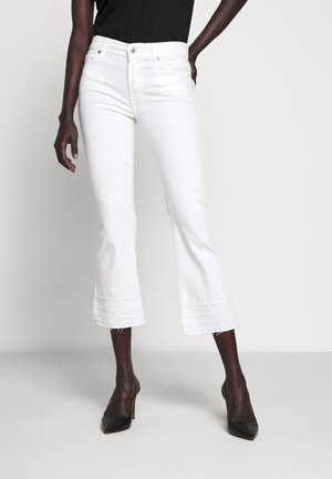 Jean blanc slim-fit court avec ourlets plissés, porté avec des talons hauts noirs pointus et un top noir.
