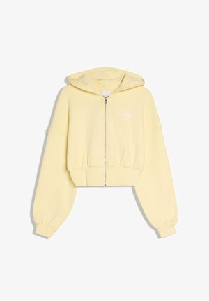 Jasnożółta krótka bluza z kapturem zapinana na zamek z przodu, z długimi balonowymi rękawami, elastycznymi mankietami oraz małym białym haftowanym logo na piersi.