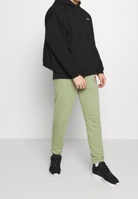 Svart huvtröja med känguruficka, tillsammans med ljusgröna sweatpants med röd textdetalj, fullbordat med svarta atletiska sneakers.