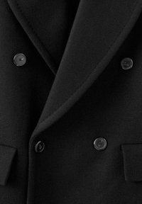 Abrigo negro de doble botonadura hecho de una mezcla de lana, con solapas anchas y cuatro botones negros, con un acabado de textura suave.