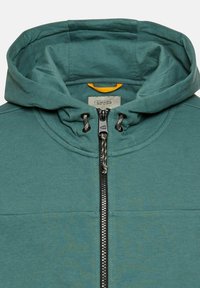 Sweat à capuche vert avec fermeture éclair à l'avant, présentant un tissu texturé, une doublure intérieure de capuche contrastante avec des détails jaunes, et des cordons de serrage ajustables.