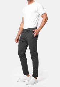 Pantalon gris à coupe ajustée, avec une texture lisse, poches avant et un détail de pli subtil, associé à un t-shirt blanc uni et des baskets blanches.
