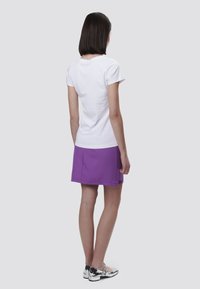 Camiseta blanca de manga corta combinada con una falda morada. El conjunto presenta un diseño sencillo y una tela suave. Zapatos plateados completan el look.