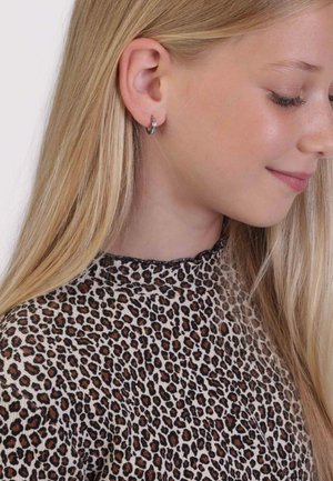 Zilveren ringoorbel met een klein blauw stenen accent, gedragen door een kind met lang blond haar, samen met een top met luipaardprint.