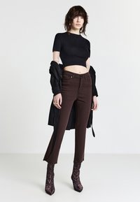 Jean marron taille haute, design ajusté, ourlets bruts, associé à un crop top noir et une veste noire, complété par des bottines à imprimé léopard.