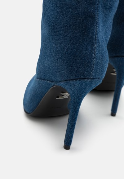 Scarpa con tacco alto in denim blu scuro, con punta a punta e tacco a stiletto sottile. Il tessuto testurizzato aggiunge interesse visivo.