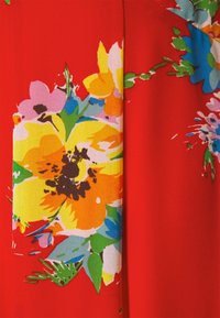 Röd tyg med livfulla blommönster i gult, rosa, orange och blått. Mjuk textur med en slät yta, som visar detaljerade bladaccenter.