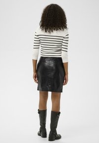 Mustat nahkainen mini hame, jossa on sileä pinta, yhdistettynä tiiviiseen valkoiseen ja mustaan raidalliseen neuleeseen sekä polvipitkiin vihreisiin saappaisiin.