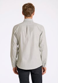 Camisa de manga larga a rayas en verde y blanco, con cuello abotonado, dobladillo curvado y detalle de pliegue en la parte posterior.