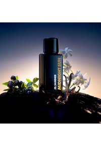 Zwarte Jil Sander Midnight Sun parfumfles omringd door bessen, witte bloemen en vanillepeulen tegen een gloeiend donkere achtergrond.