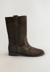 Botte en suède marron montante avec un bout arrondi, semelle en caoutchouc plate et une languette à l'arrière. Texture lisse avec des détails de couture subtils.