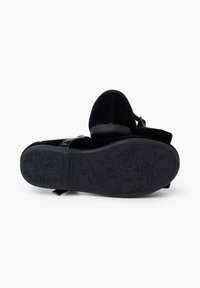 Sandalia de terciopelo negro con suela acolchada, correa ajustable y detalles de patrón floral en la suela exterior. Diseño de punta redonda y tacón bajo.