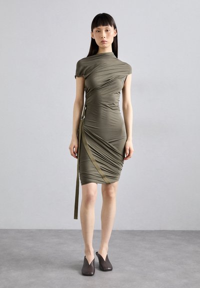 Rochie ajustată, de culoare verde măslin, cu guler înalt, mâneci scurte și design drapat. Include o curea laterală și este asortată cu pantofi maro închis.