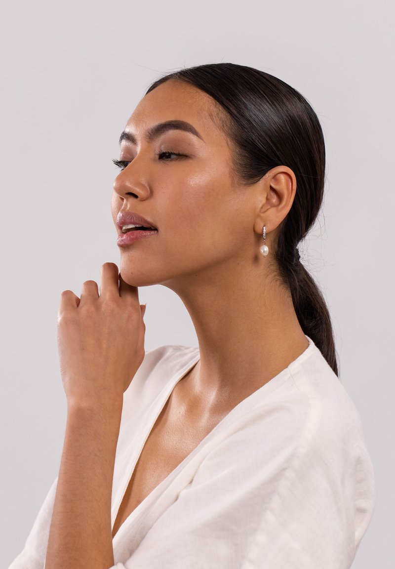 Silberne Tropfohrringe mit einer Perle, die an einem zarten Ring hängen. Das Modell trägt eine hellfarbige Bluse und zeigt einen natürlichen Schimmer.