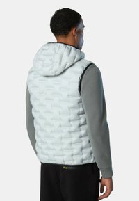 Weiße gepolsterte Weste mit Kapuze, die ein gestepptes Design aufweist. Getragen über einem grauen Langarmshirt, zeigt sie eine enge Passform und eine strukturierte Oberfläche.