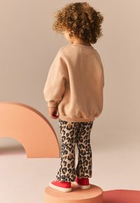 Beżowy sweatshirt z balonowymi rękawami, połączony z brązowymi i czarnymi legginsami w lamparcie cętki oraz czerwonymi trampkami.