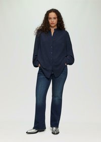 Navy-blaues Hemd mit Kragen, strukturiertem Stoff und voluminösen Ärmeln, kombiniert mit dunkelblauen Schlagjeans und silbernen Ankle Boots.