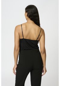 Svart satin cami med tunna remmar, kombinerad med högmidjade svarta byxor. Slät textur och minimalistisk design.