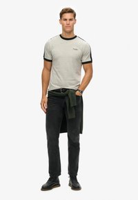 Grå kortærmet t-shirt med sorte detaljer, parret med sorte jeans og sorte snørebåndsstøvler. En grøn sweater bundet om livet.