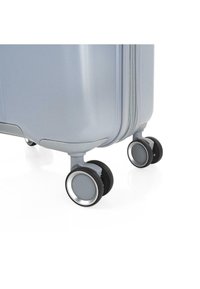 Maleta rígida de color azul claro con superficie texturizada, que cuenta con dos ruedas giratorias con acentos plateados para facilitar la movilidad.