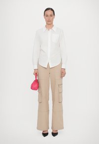 White button-up shirt with a chest pocket, beige cargo pants with side pockets and a zip, and a small pink handbag. Black pointed heels.