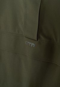 Tissu vert olive en gros plan avec des lignes de couture verticales et horizontales subtiles et un petit logo réfléchissant "aimn" centré.