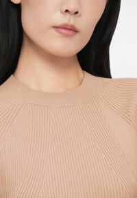 Sweater de malha canelada em bege claro, com decote redondo e detalhes texturizados nas mangas e no corpo. Material de malha suave e design ajustado.